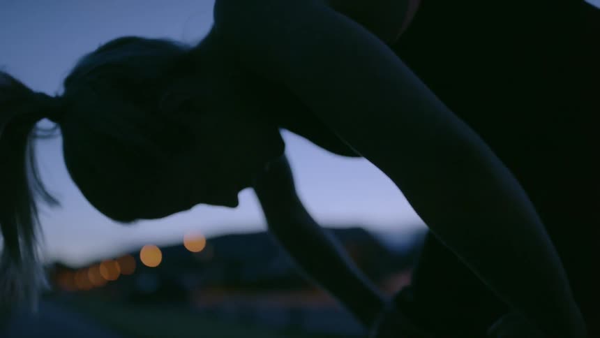 A woman bends over to catch her breath outside at dusk