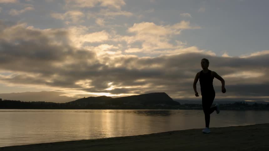 A woman is running along the shore at sunset