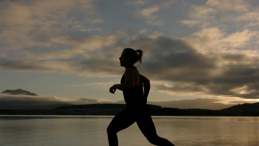A woman is running by a lake at sunset