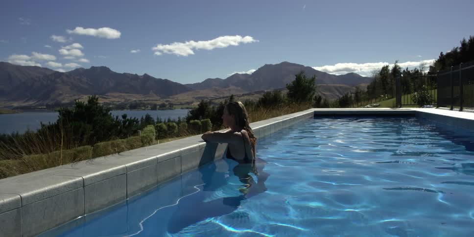 A woman stands in a swimming pool overlooking a mountain lake