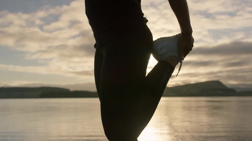 A person dressed in workout gear stretches near the ocean