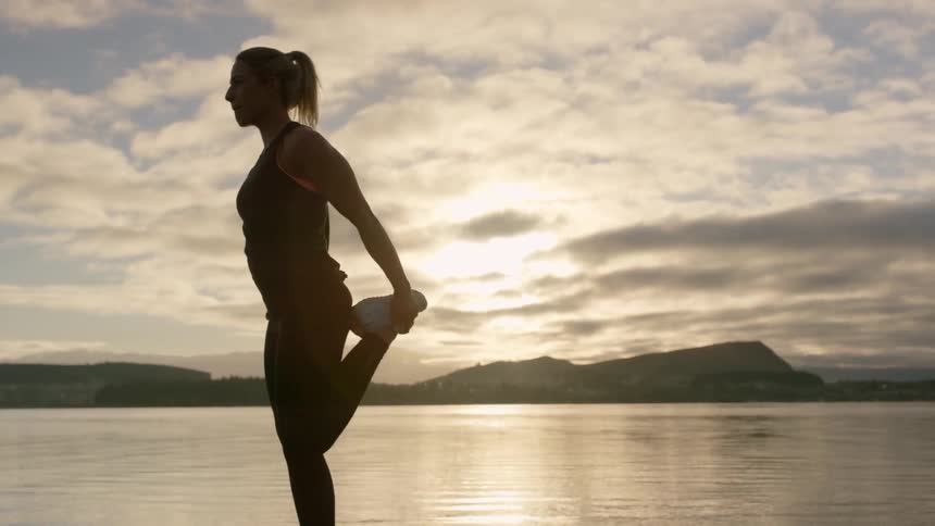 A woman stretches by the lake at sunrise
