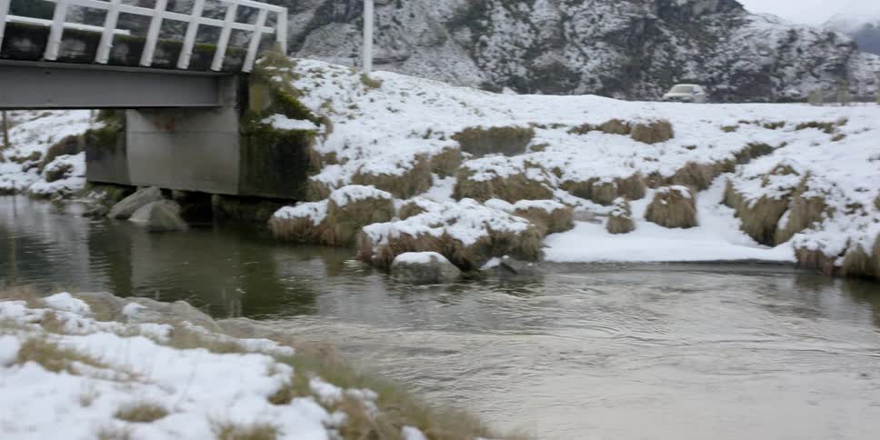 Stream flows under a bridge surrounded by snowy landscape
