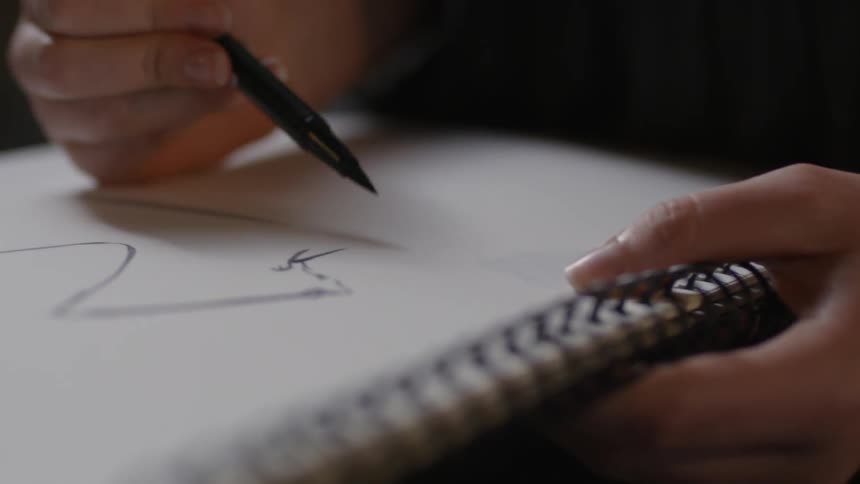 A woman sketches in a notebook with a marker