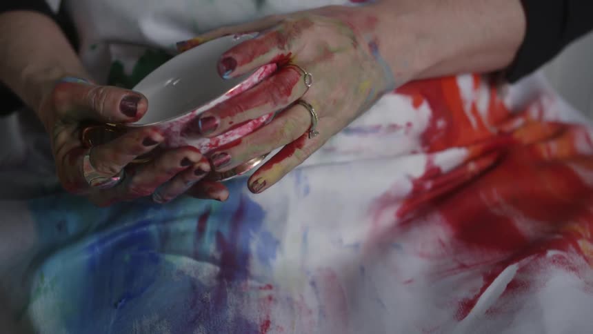 A person holds a cup with paint all over her hands