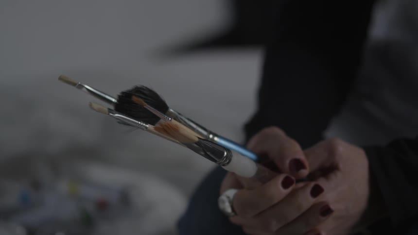A person is holding a bunch of paint brushes
