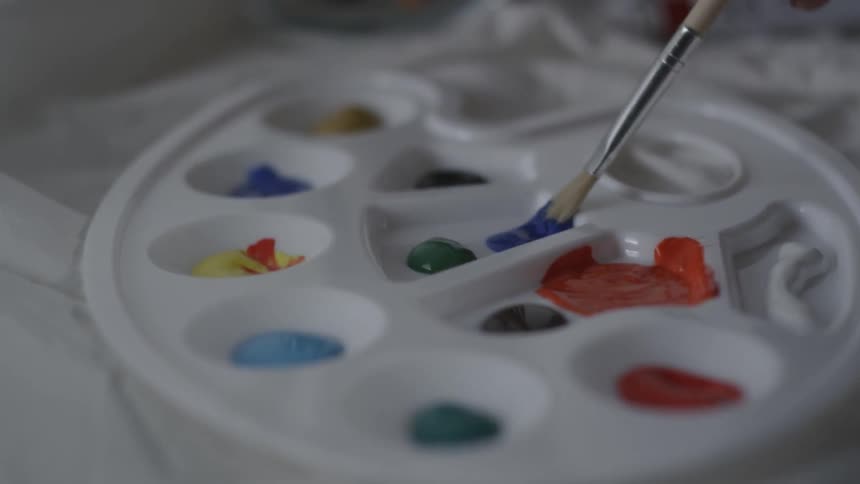 Brush dabs blue paint on a palette