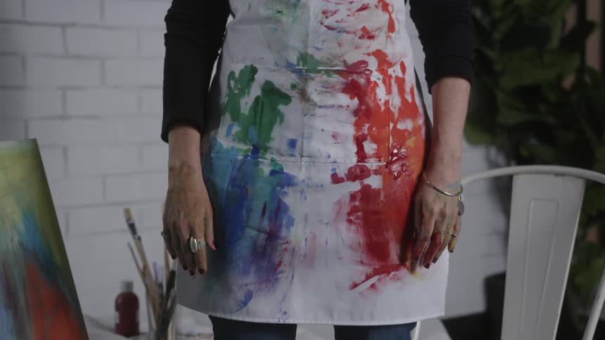 Woman standing still wearing a smock smeared with paint