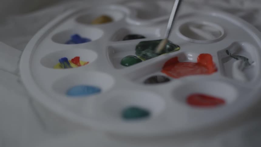 An artist mixes paint on a palette with a paintbrush