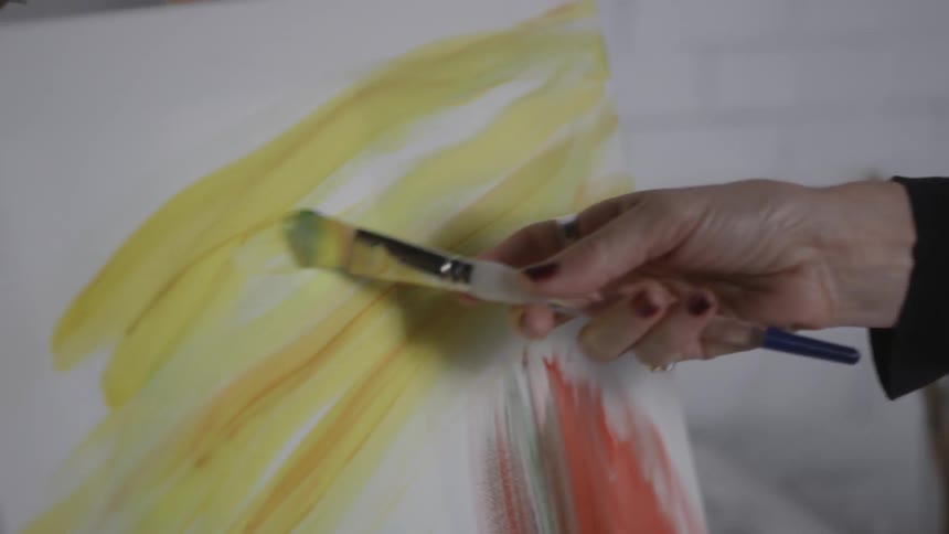 Person brushing yellow paint onto a canvas