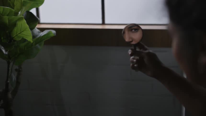 A woman looks at her reflection in a small hand mirror