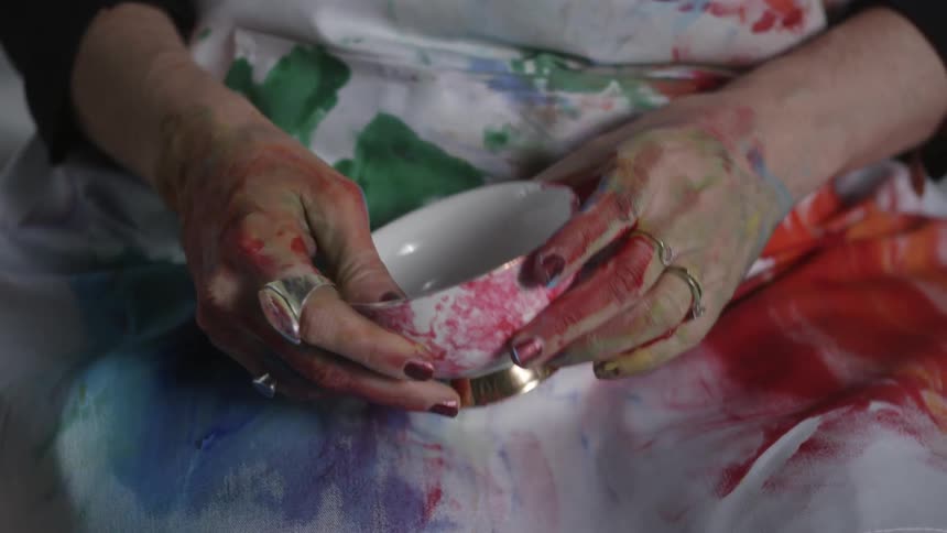 Woman with paint covered hands holds a paint covered mug