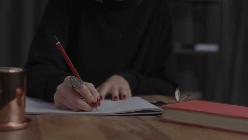 A person is writing with a pencil in a notebook