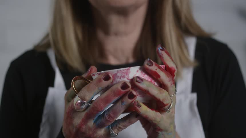 Woman with paint covered hands holds a paint covered mug