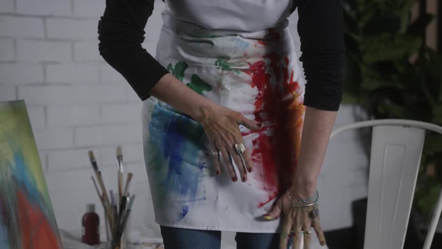 A woman wipes paint from her hands on her white apron