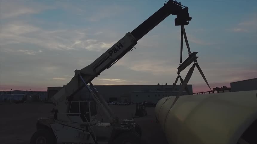 A crane moves a large cylinder outside a warehouse