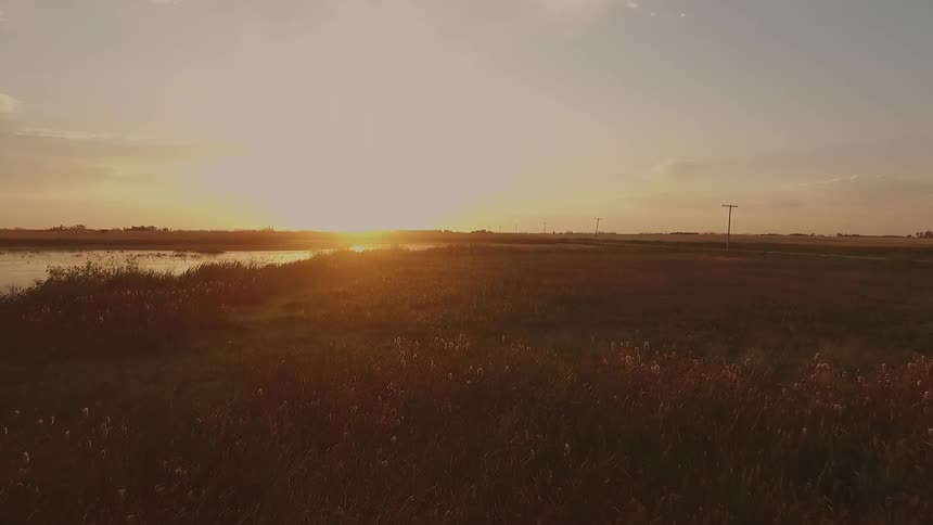 The sun sets over a lake and grassy field