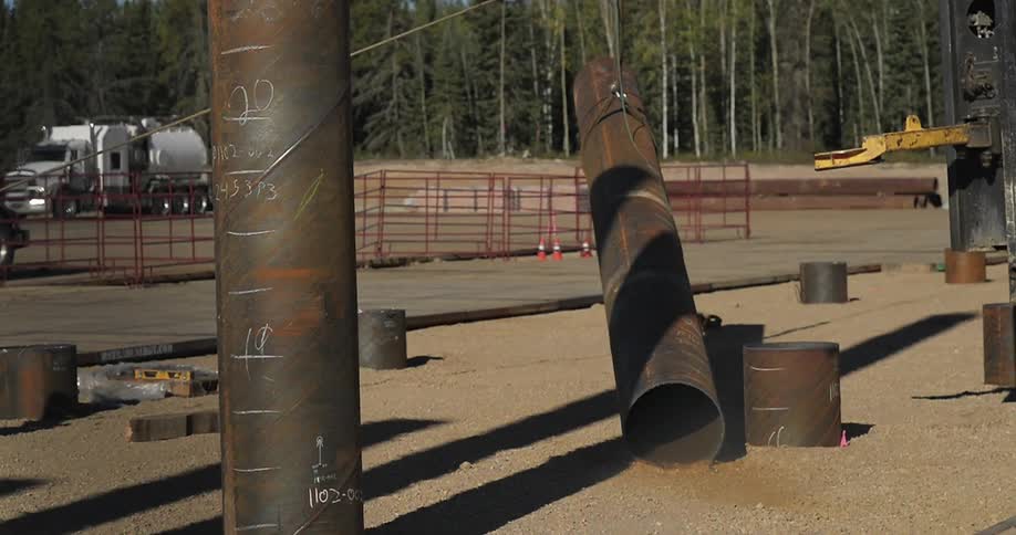 A crane moves a large metal pipe