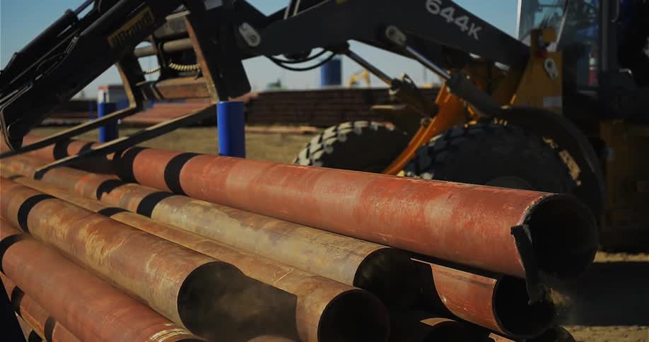 A forklift drops a metal pipe onto a stack of pipes