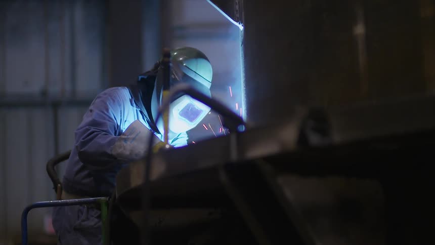 Person wearing a helmet welds with sparks flying around
