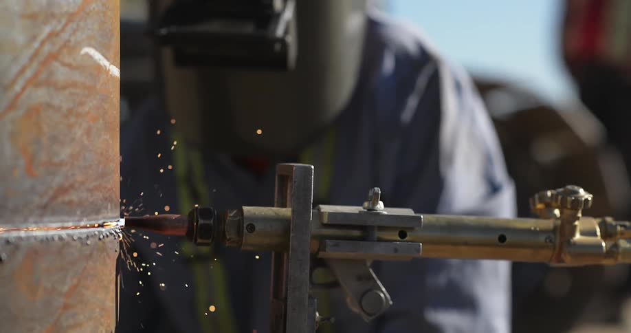A worker is cutting a metal tube with a torch