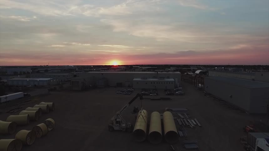 The sun sets over a work site with pipes and cranes