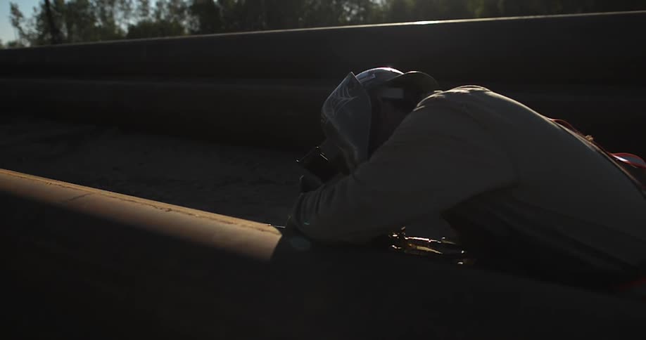 Person welds a large pipe outside on a sunny day