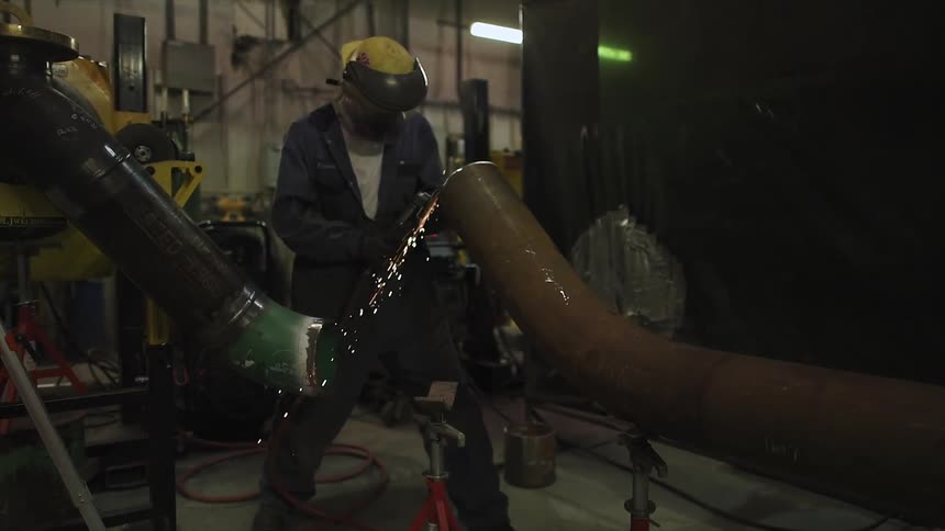 A worker is cutting the side of a pipe with a torch