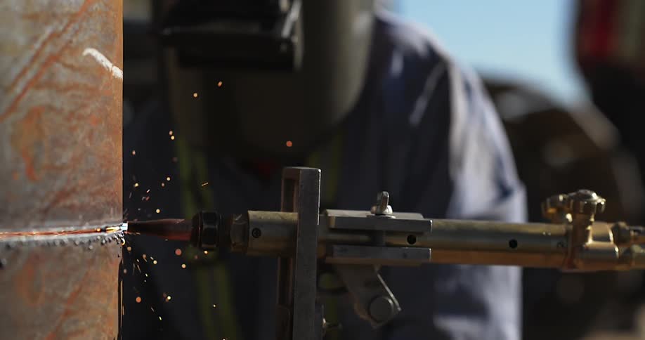 A welder works on a metal pipe as sparks fly