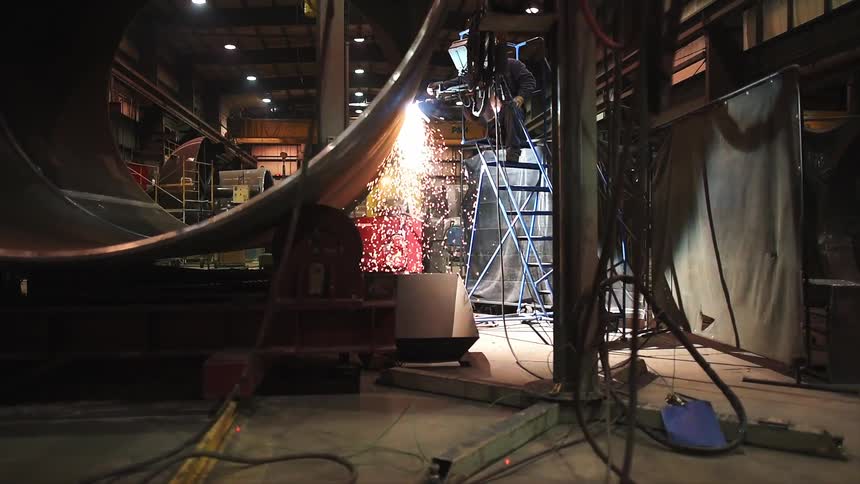 A worker is on a ladder welding in a warehouse
