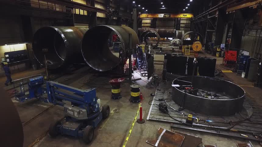A welder works on a large metal cylinder in a factory