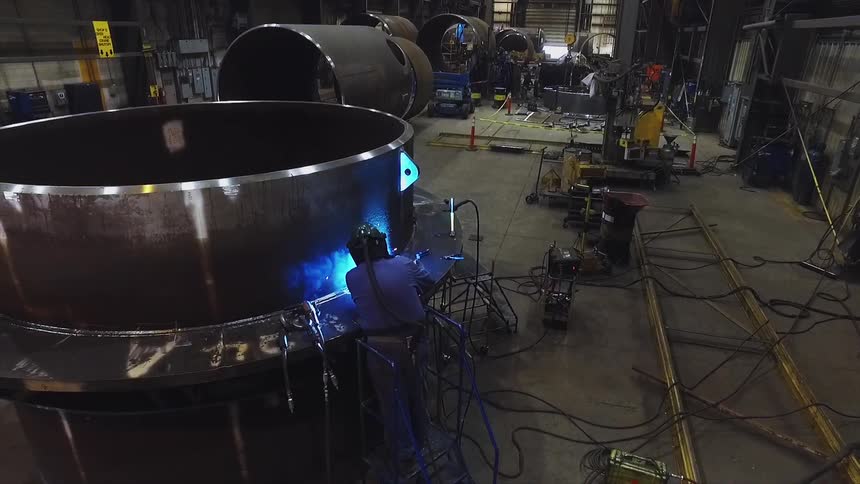 A welder works on a large metal tank in a factory