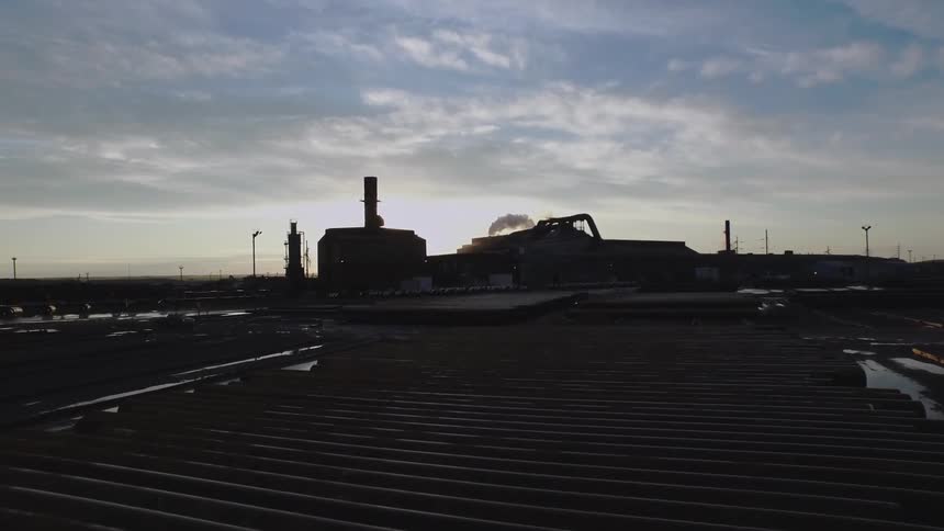 Smoke billows out of a large factory at the edge of a city