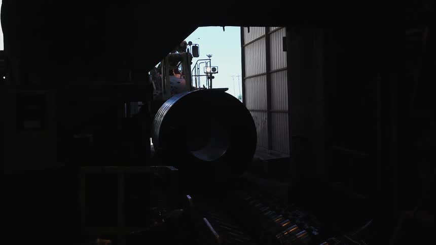 Tractor pushes a large metal tube into a building