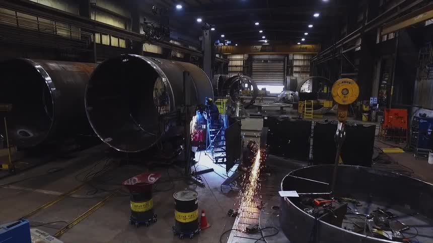 A welder works on a large metal cylinder in a factory as sparks fly around
