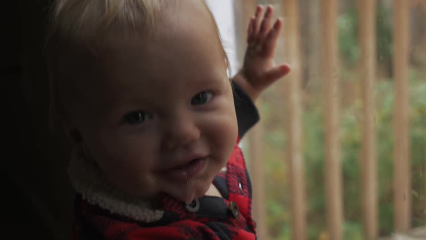 A baby is smiling with his hands on the window