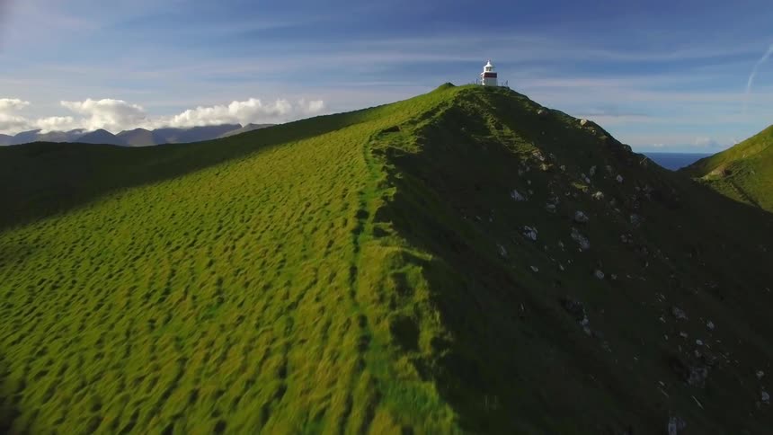 A person walks up a mountain ridge towards a building