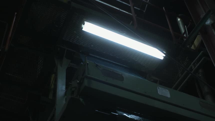 A fluorescent light shines in a dark factory setting