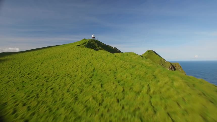 A lighthouse sits perched on a green cliffside overlooking the ocean