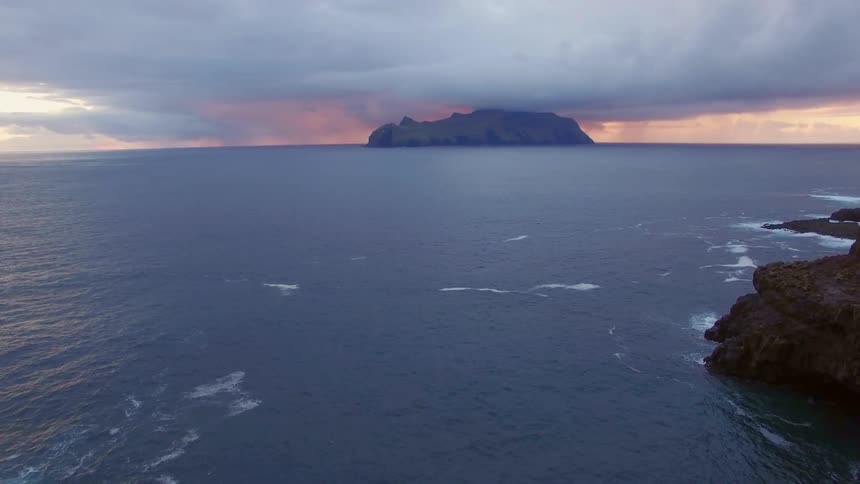 Person sits on a bench at the edge of a cliff overlooking a body of water