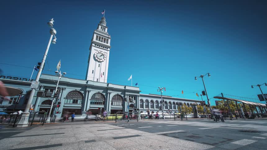 People travel along a square near a clock tower
