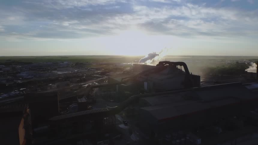 Smoke billows out of a large factory at the edge of a city