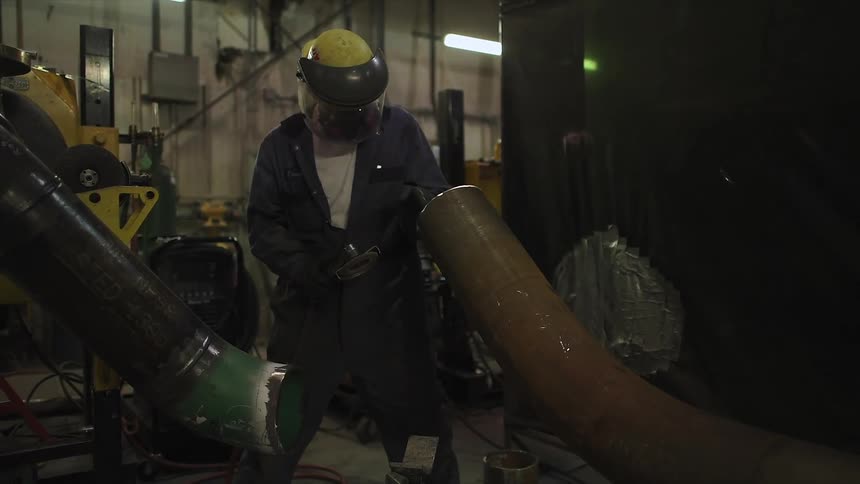 Man welds a large pipe in a workshop
