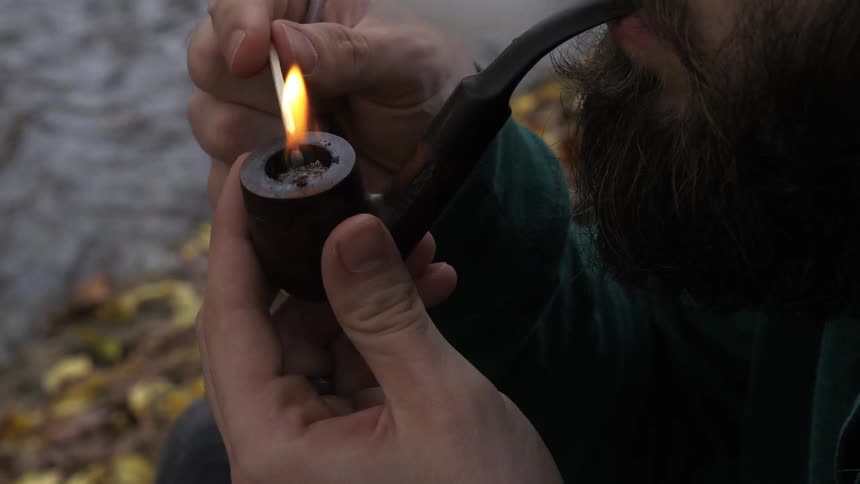 Person lights a pipe with a match at the edge of water