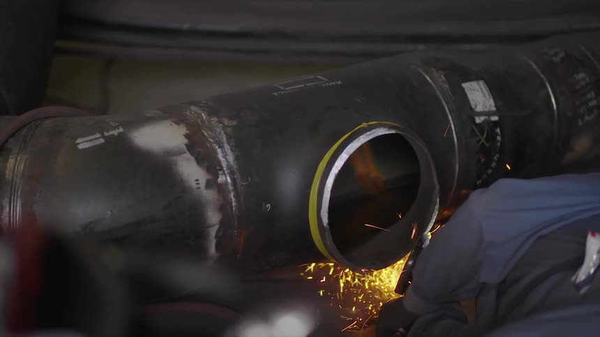 A worker uses a power tool to grind a metal pipe as sparks fly