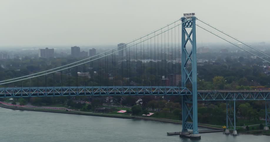 A blue bridge over a large river with a city in the background