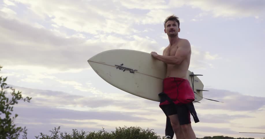 Man carrying surfboard on a windy day