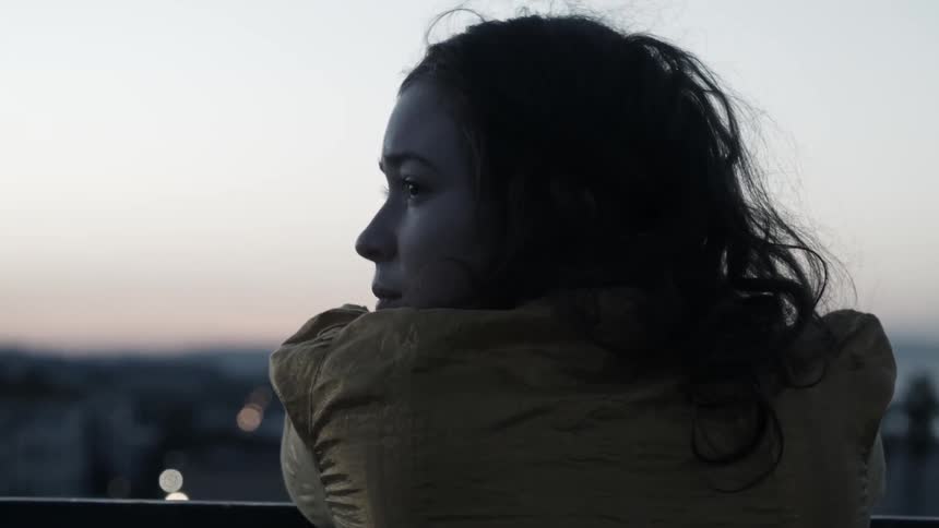 A woman looks out over city buildings at sunset