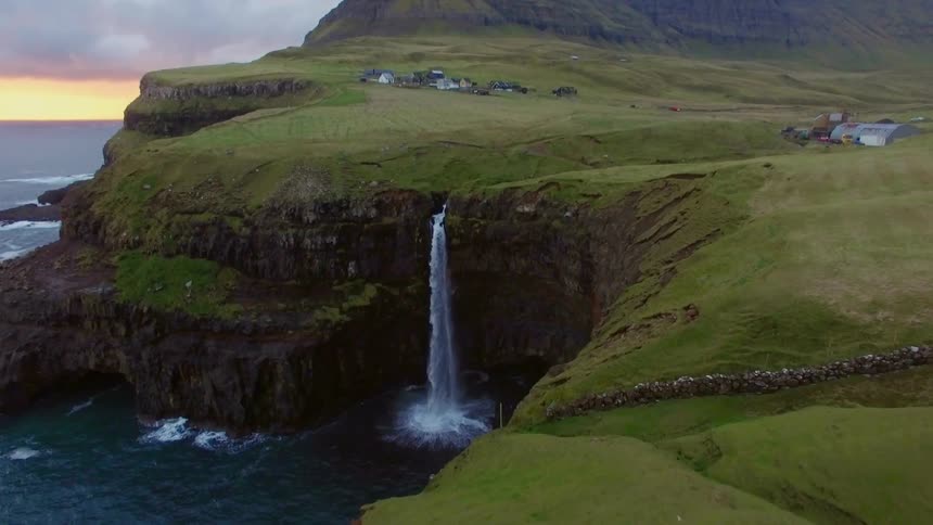 Person stands at the edge of a cliff overlooking a body of water