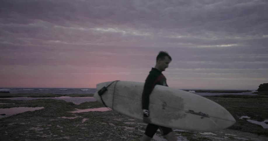 Man carrying a surfboard away from the water